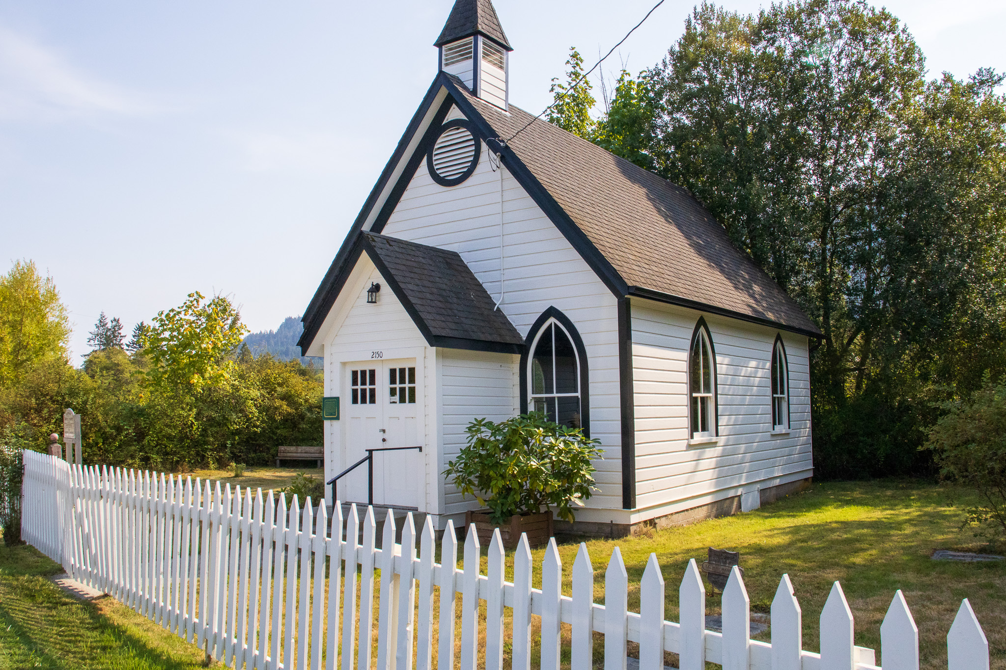 The historic Burgoyne United Church - a white and black single level house with a steeple in a white picket fenced yard.