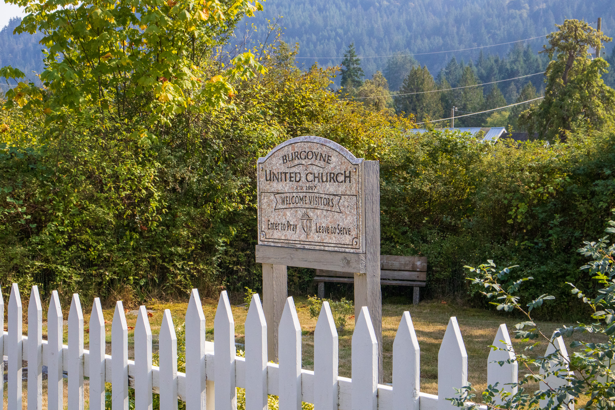 A historic church sign in the picket fenced yard.