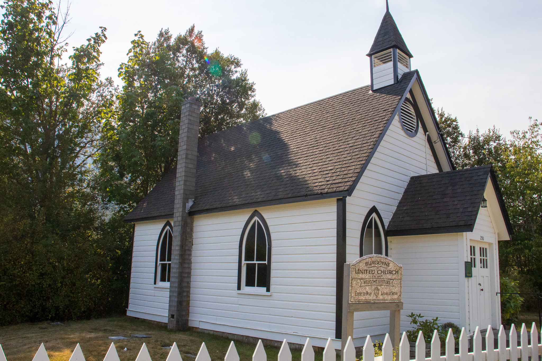 The historic Burgoyne United Church - a white and black single level house with a steeple in a white picket fenced yard.